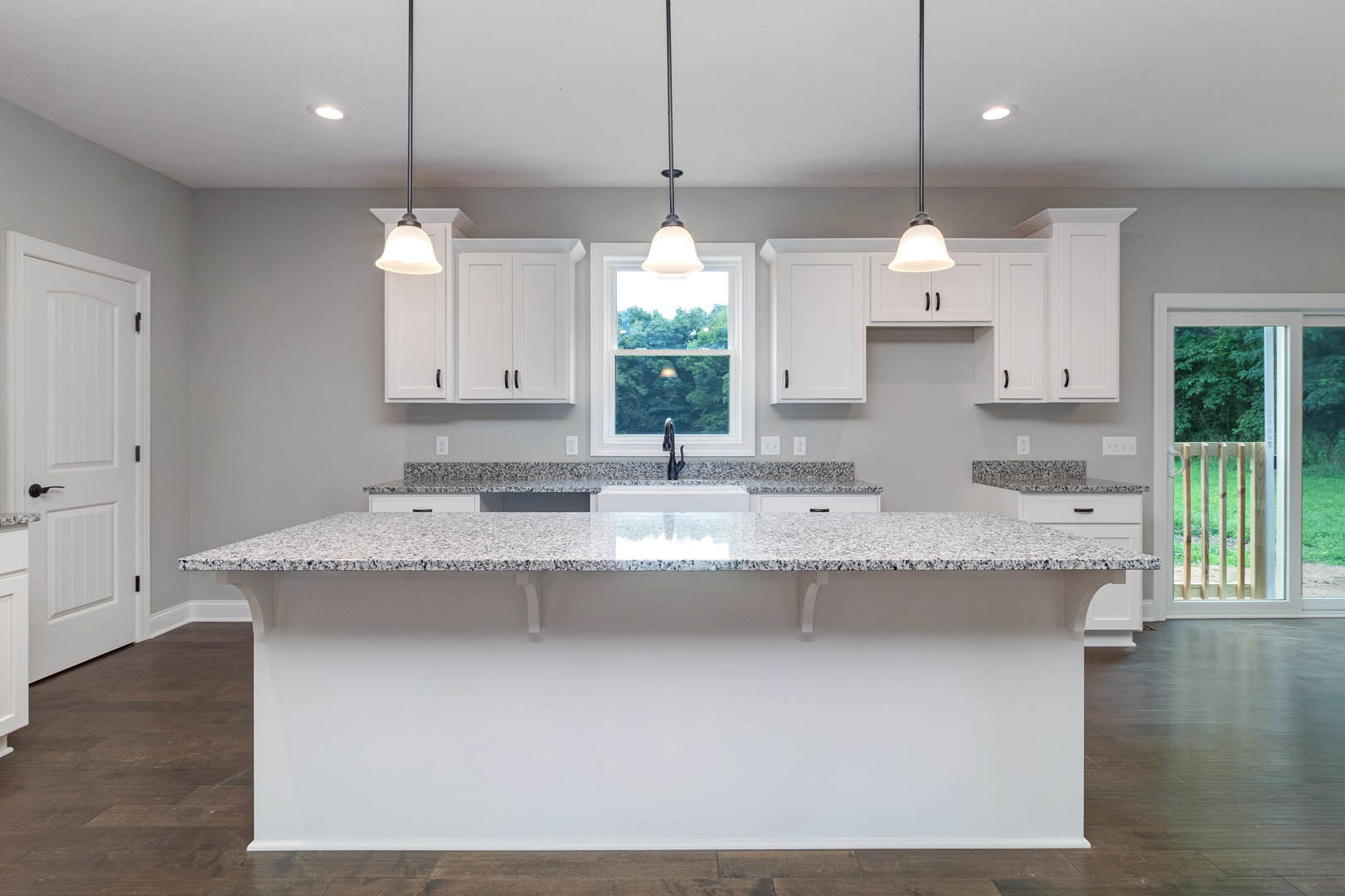 Marble kitchen countertop with white tile backsplash, white cabinetry, stainless steel sink and tap, black handle on white door, wooden railing, woman standing near window, toilet
