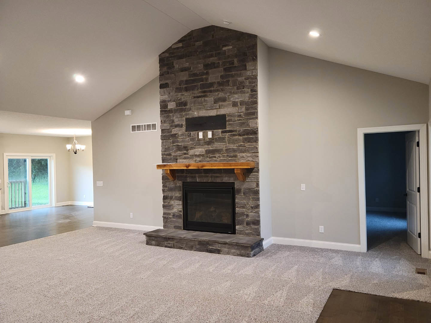 Stone fireplace with glass window and wood mantel, sliding glass door with white frame opening to adjacent room, stone step visible on porch, hardwood flooring and neutral walls in
