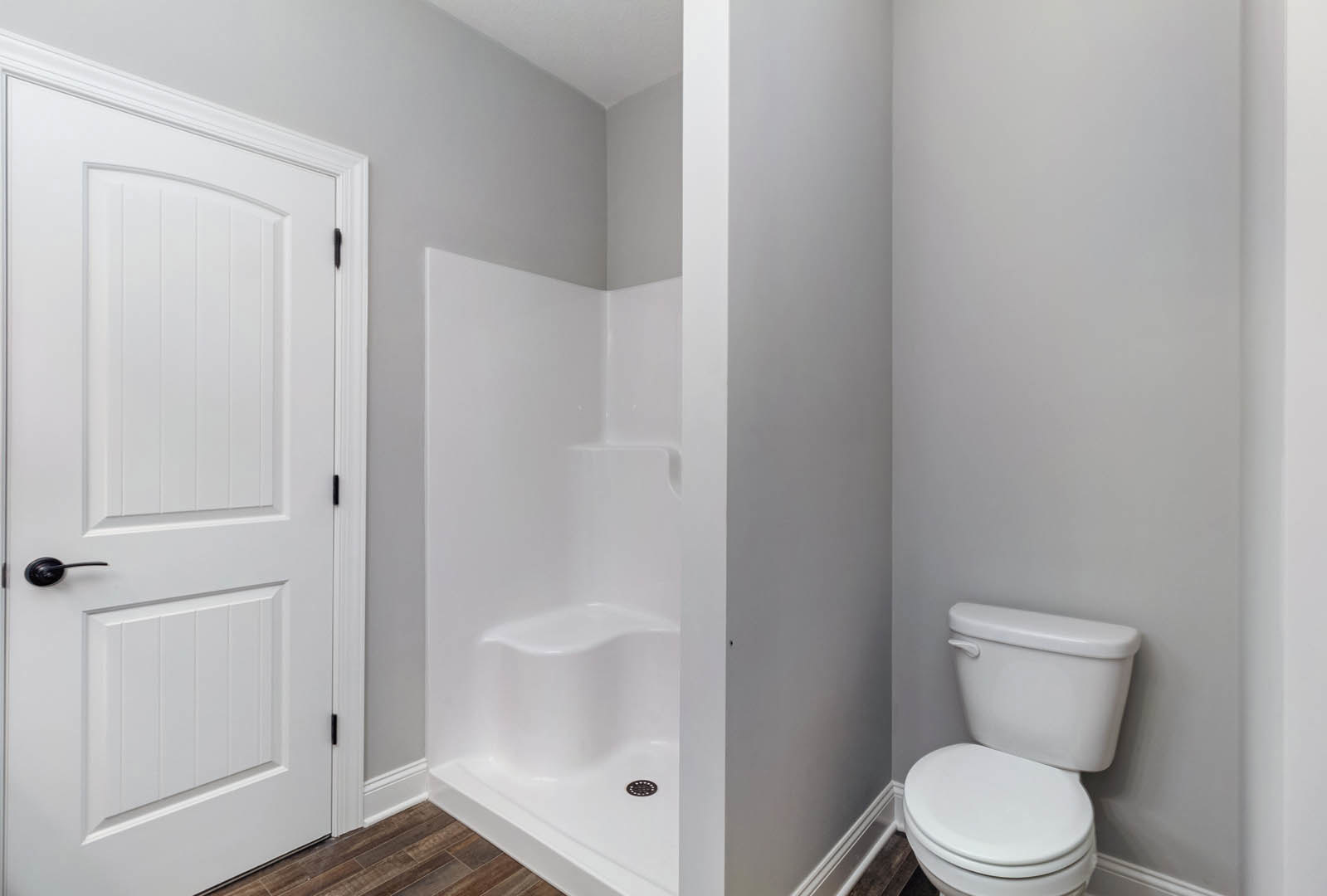 Bathroom with white toilet, glass-enclosed shower, light tile flooring, white walls, and a white door with black handle