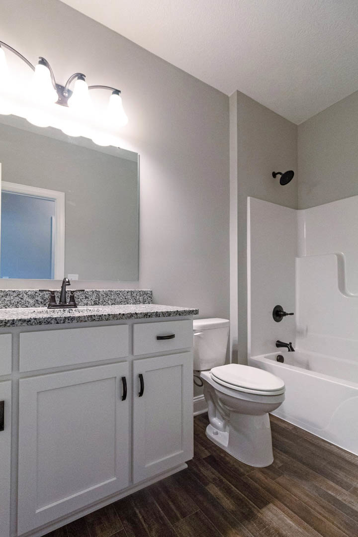 Bathroom with marble countertop, white cabinetry with black handles, toilet, white door, and modern light fixture