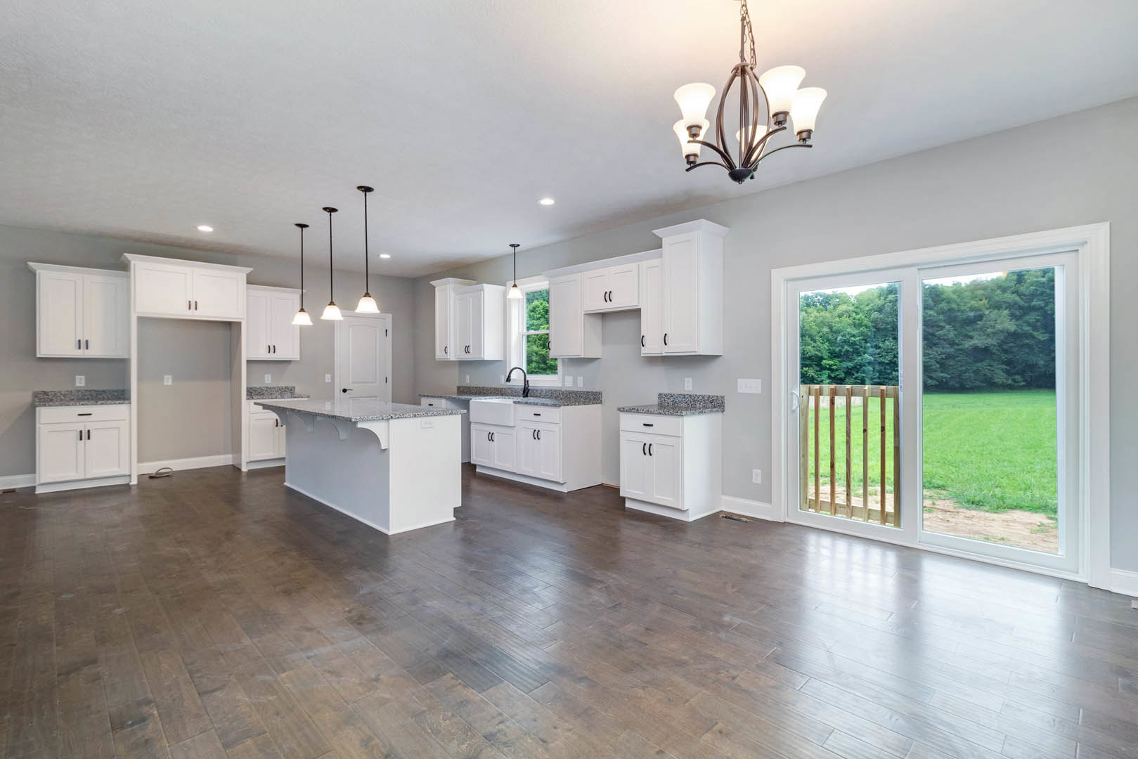 Open kitchen and dining area featuring white cabinetry, granite countertops, hardwood flooring, a central kitchen island, and sliding glass doors leading to a fenced backyard.
