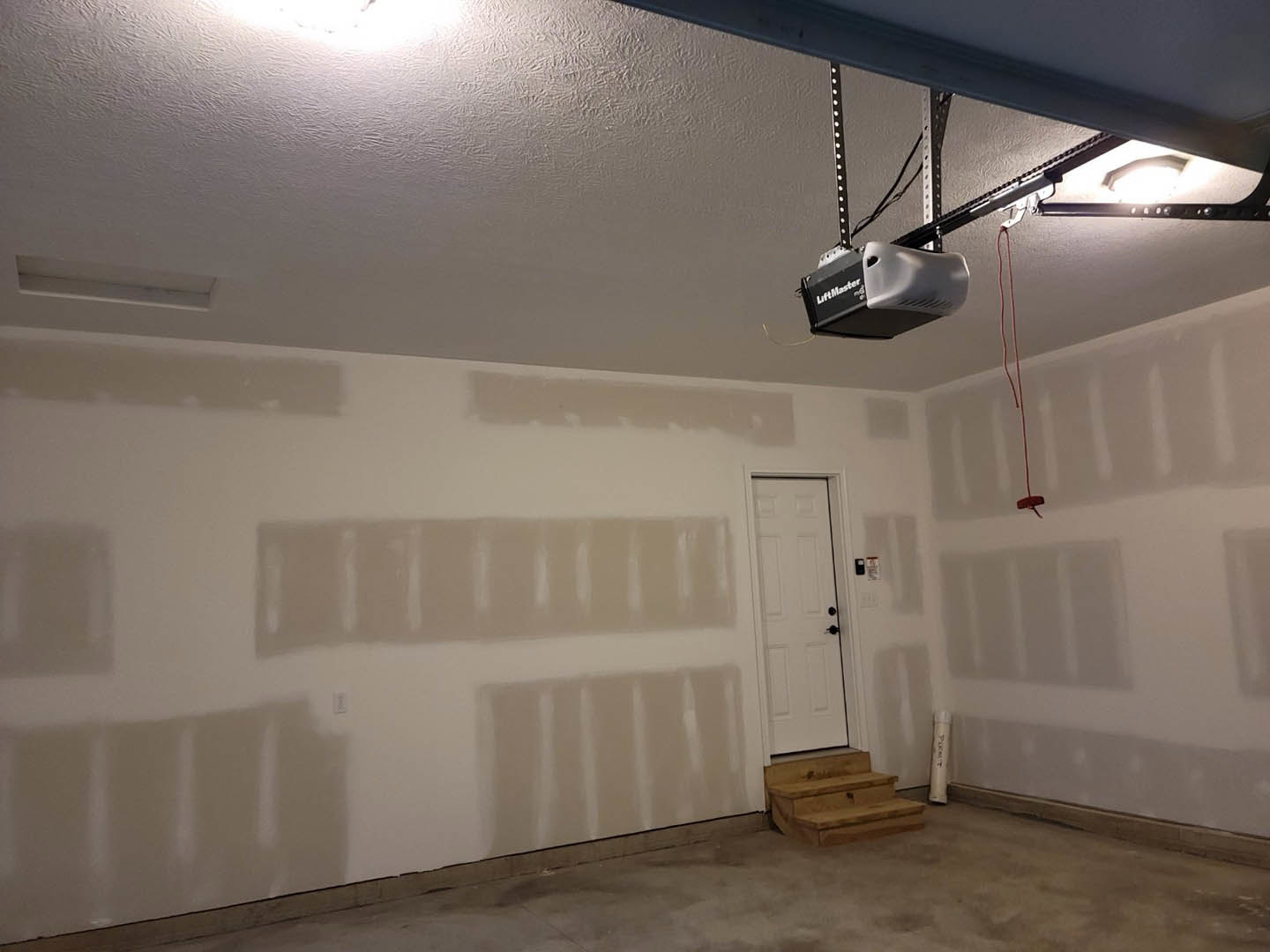 White plaster walls, white door with black hardware, wooden staircase, light ceiling fixture, hardwood flooring