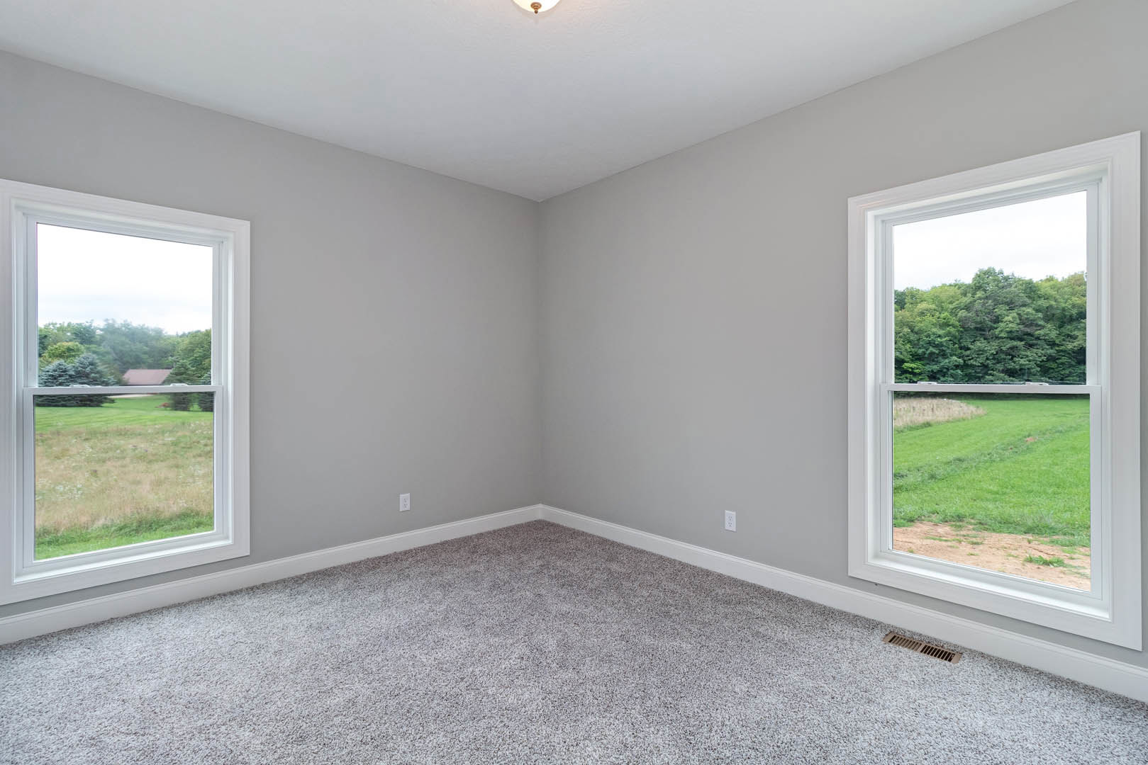 Carpeted room with large windows overlooking grassy field and trees, white ceiling with recessed light fixture