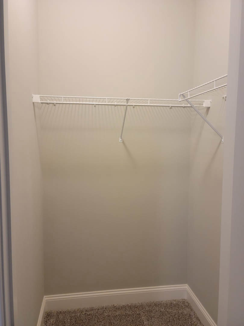White closet with built-in shelf and metal hanging rods, carpeted floor, white plaster walls.