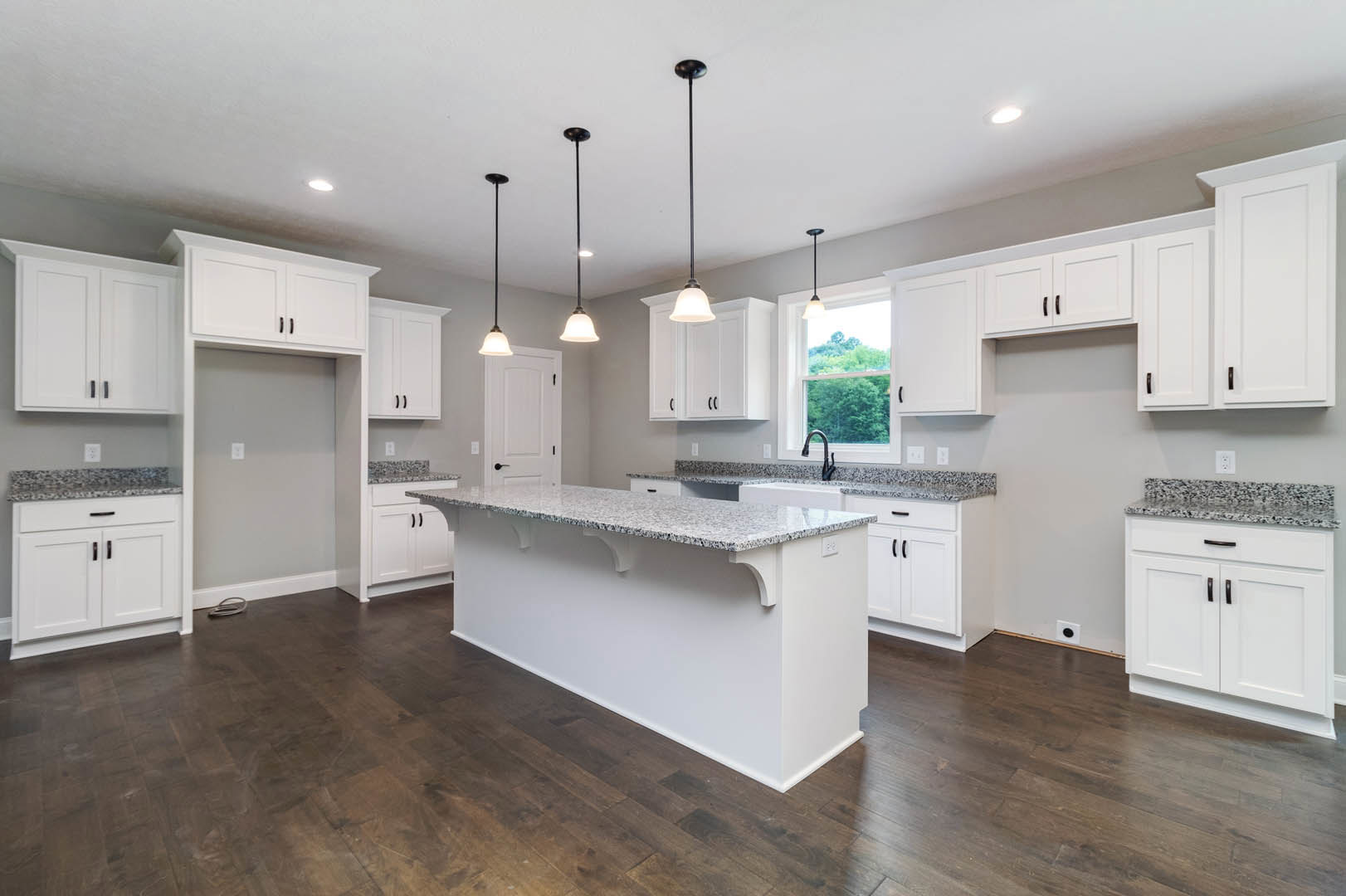 White kitchen cabinets with black handles, marble countertop, stainless steel sink, modern light fixture with white shade, neutral walls, and hardwood flooring.