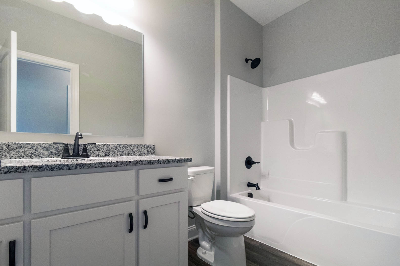 White bathtub and toilet against tiled wall, black light fixture above, chrome faucet, white cabinetry, and door partially visible.