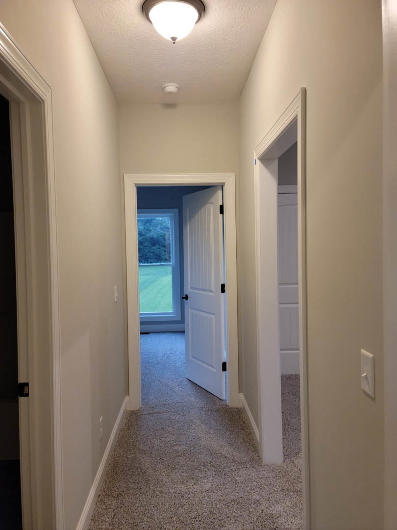 Carpeted hallway with white door and glass door, plaster walls, ceiling, and window overlooking green field