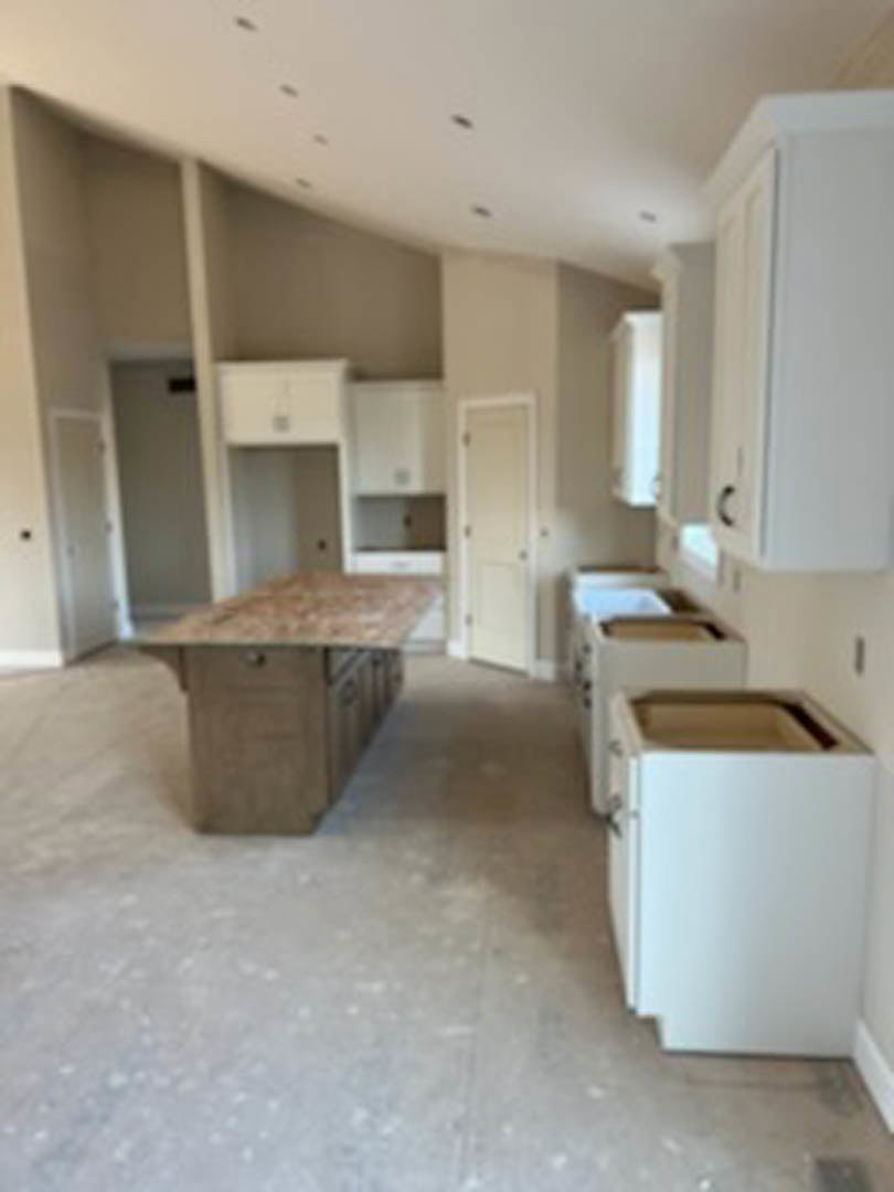 White shaker cabinets with brushed nickel hardware, light wood countertop, stainless steel sink, neutral tile backsplash, and hardwood flooring in a modern kitchen.