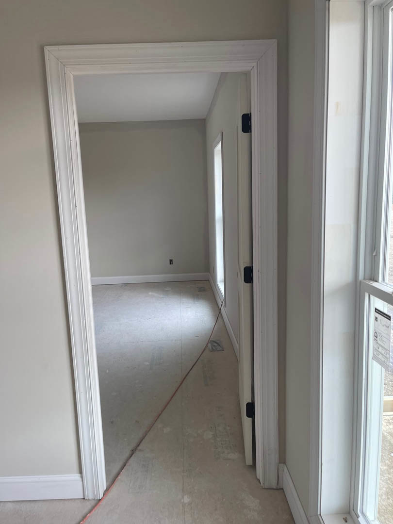 White plaster wall with doorway, red wire hanging near ceiling, light wood flooring, and window trim visible