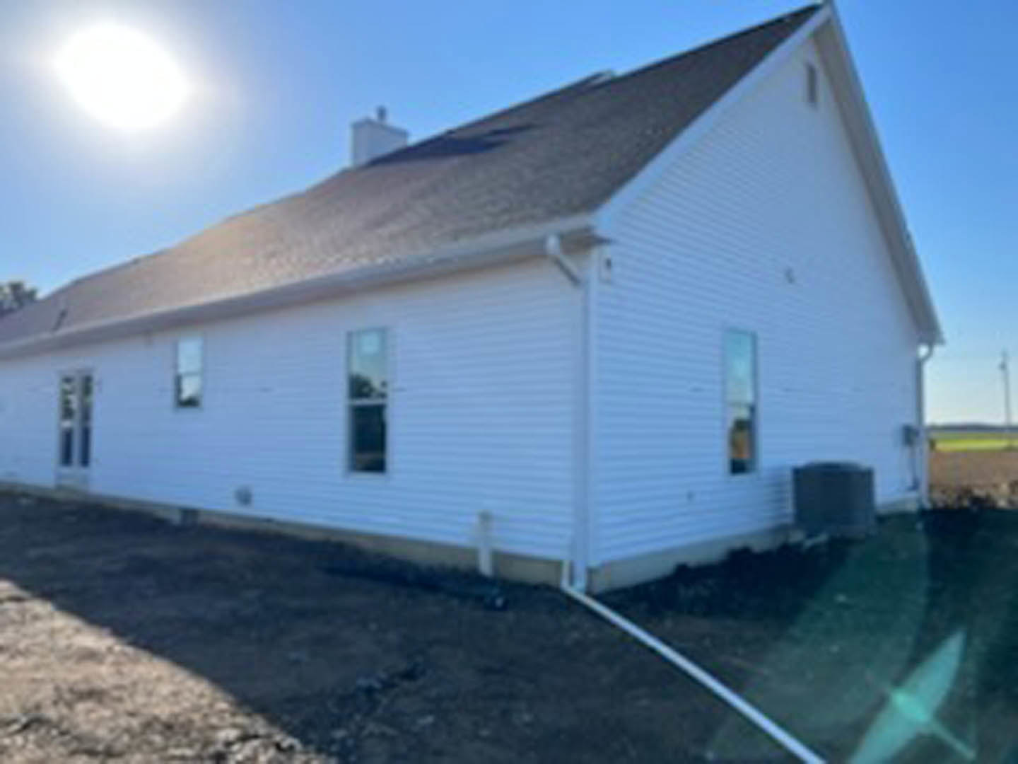 White house with light siding, shingle roof, and dirt yard under clear blue sky