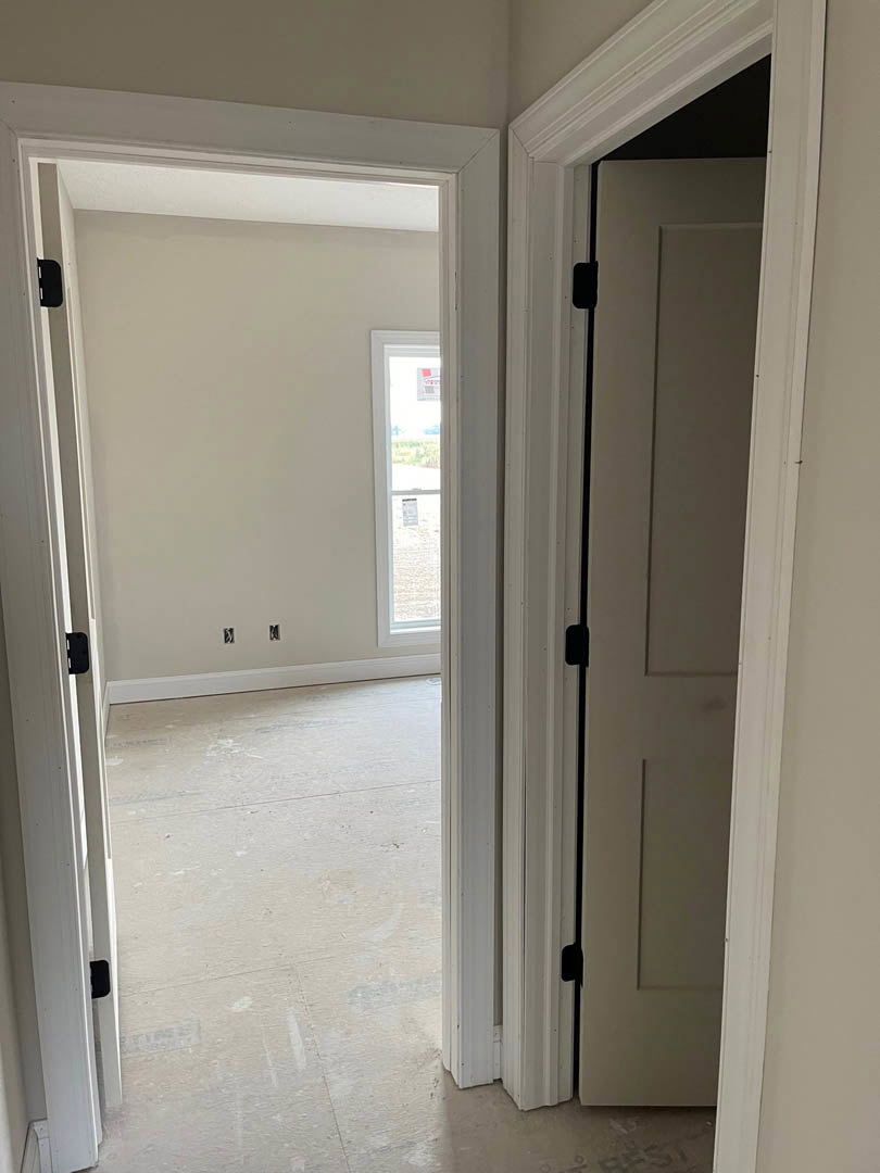 White-walled room with open white door featuring black handle, white flooring, and window displaying a sign