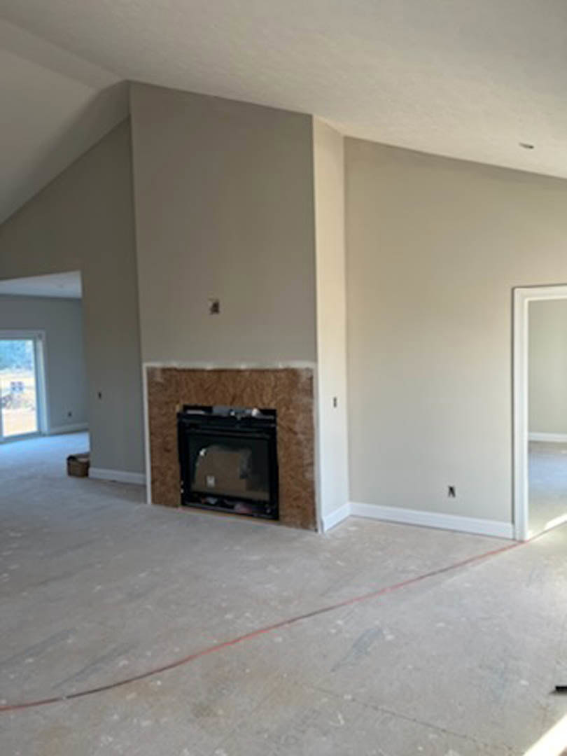 Stone fireplace with white mantel set against smooth plaster wall, hardwood flooring, and recessed ceiling lights in spacious living room