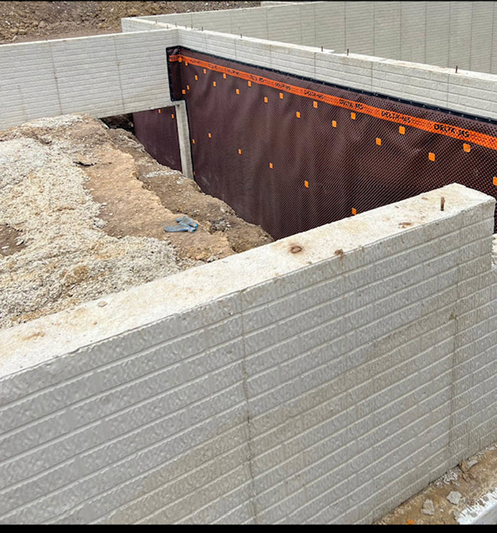 Concrete wall and metal fence at residential construction site, dirt ground with scattered materials, blue tarp partially visible.