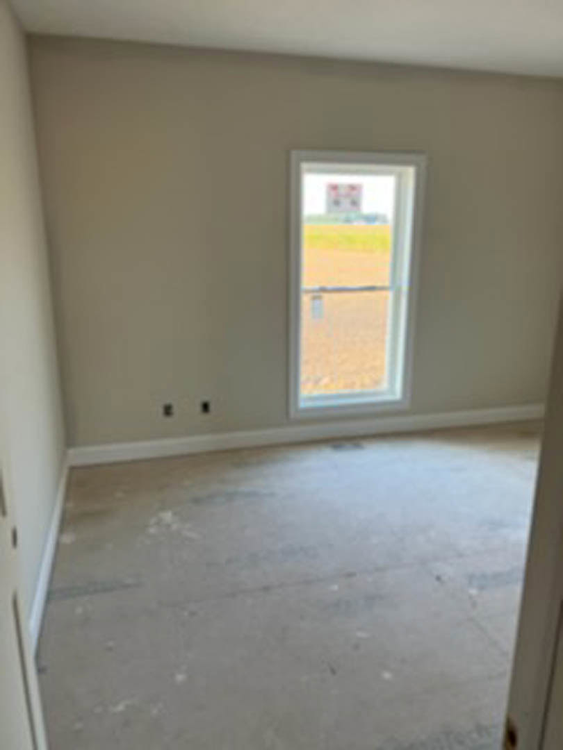 White-painted concrete floor in a minimalist room featuring a large window overlooking a grassy field, plaster walls, and a simple ceiling.