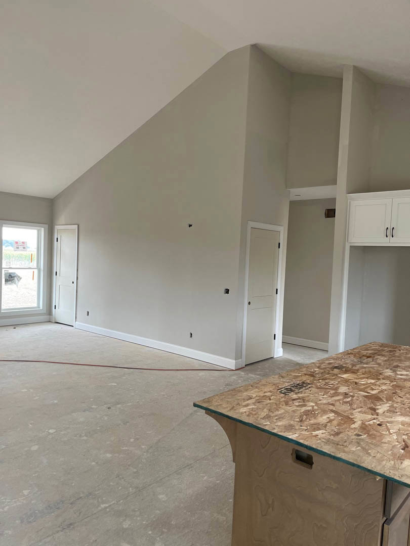 Glass-top table centered in a room with light plywood flooring, white plaster walls, white door featuring black handles and knobs, window with a sign, and minimalist cabinetry.
