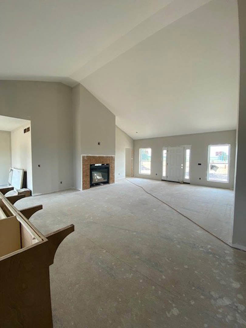 Living room with brick fireplace, upright piano, white door, wood flooring, plaster walls, and large window.