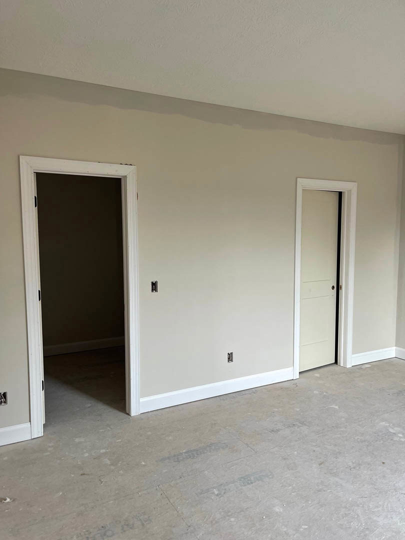 White door with black frame set in dark accent wall, adjacent to second door, light wood flooring, white ceiling, minimalist interior finishes