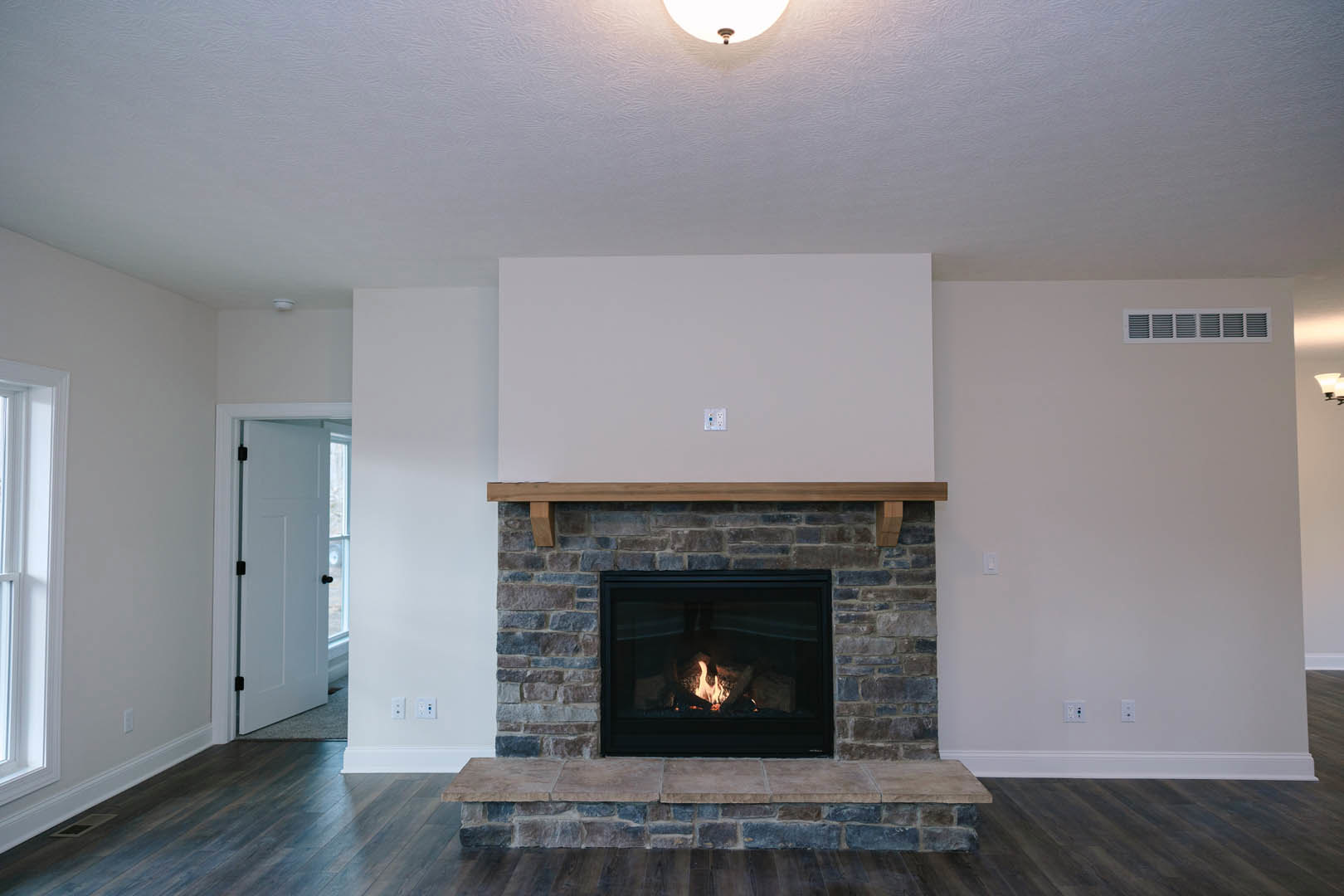 Brick fireplace with burning fire set against a white wall, wood flooring, and adjacent window in a cozy living room.