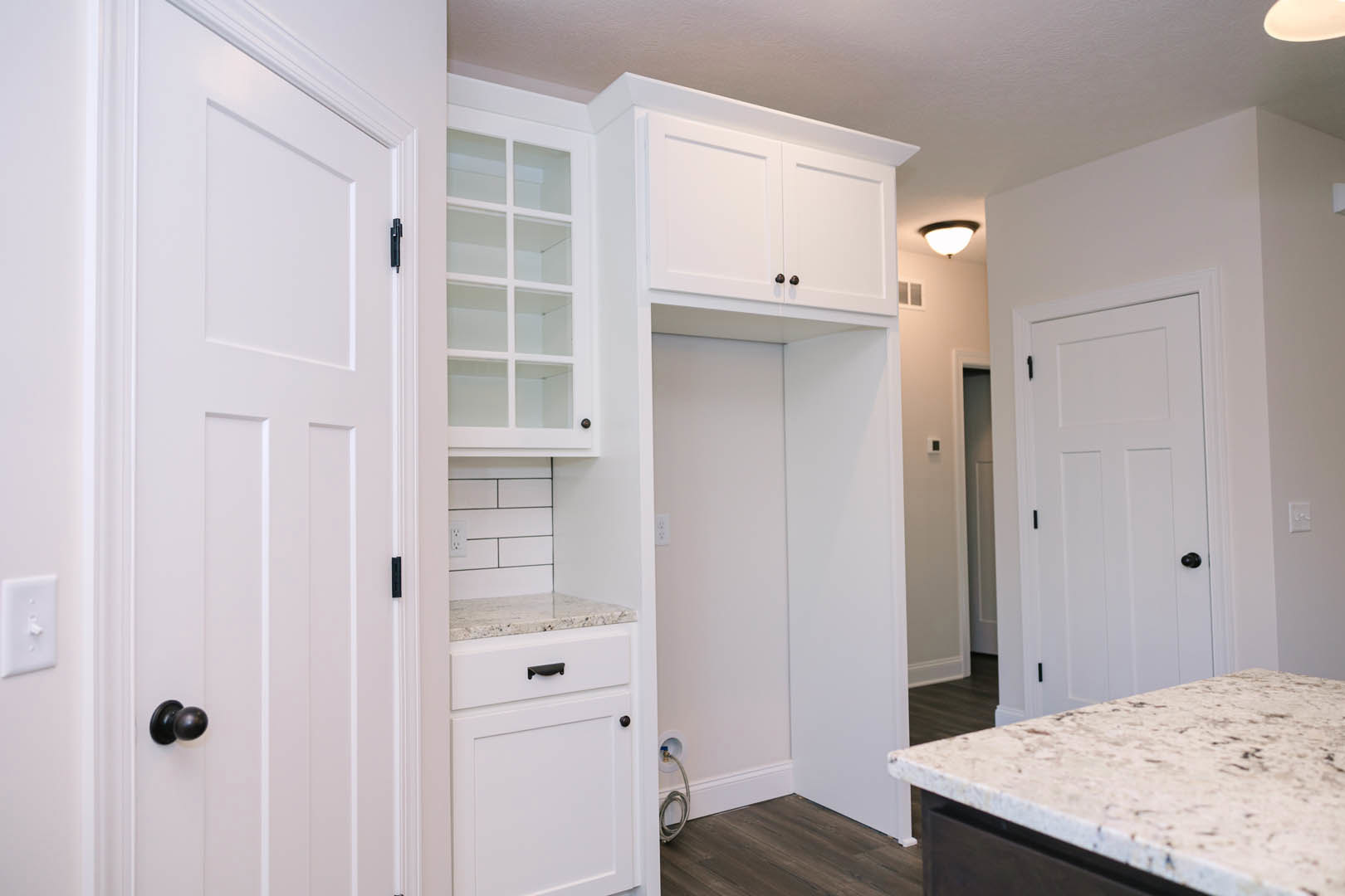 White kitchen cabinets with glass panes, marble countertops, black hardware, and a white door in the background