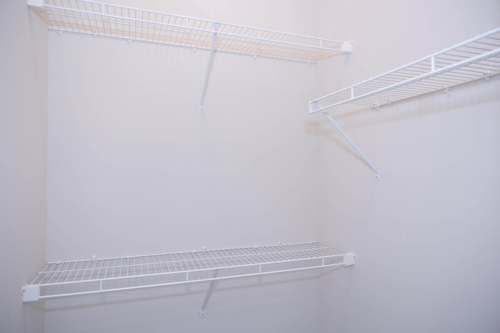 White metal shelving mounted on a smooth white wall in a minimalist room interior.