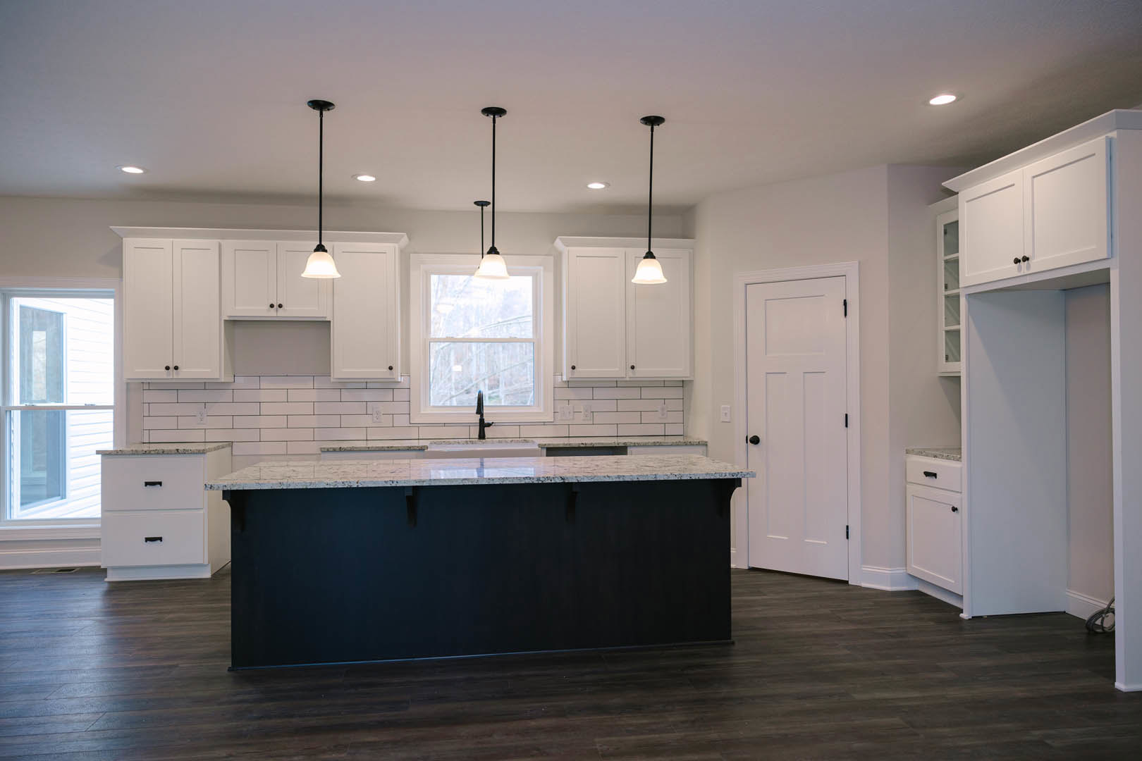 Black kitchen island with white cabinets, white drawers and doors featuring black handles, white-framed window, light fixture above, neutral walls and flooring
