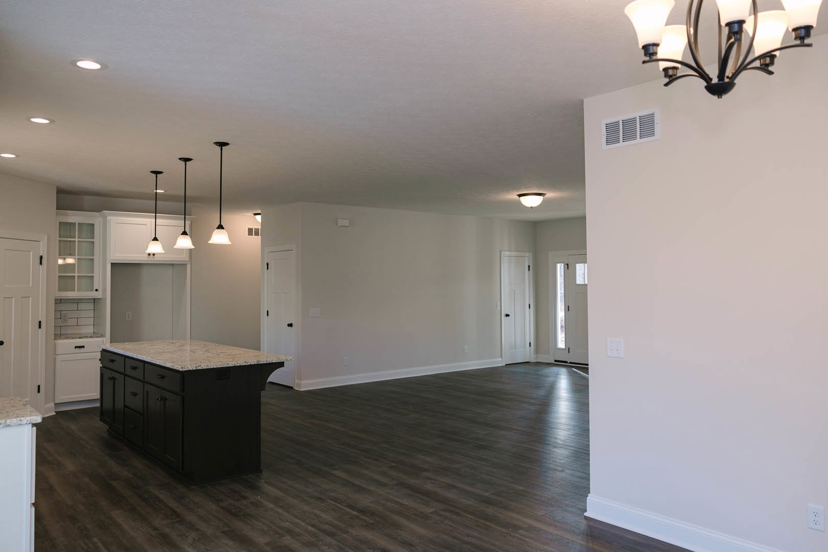 Open kitchen and dining area with light wood floors, marble-topped island, white cabinetry, modern chandelier, white door with black hardware, vent and decorative black text on