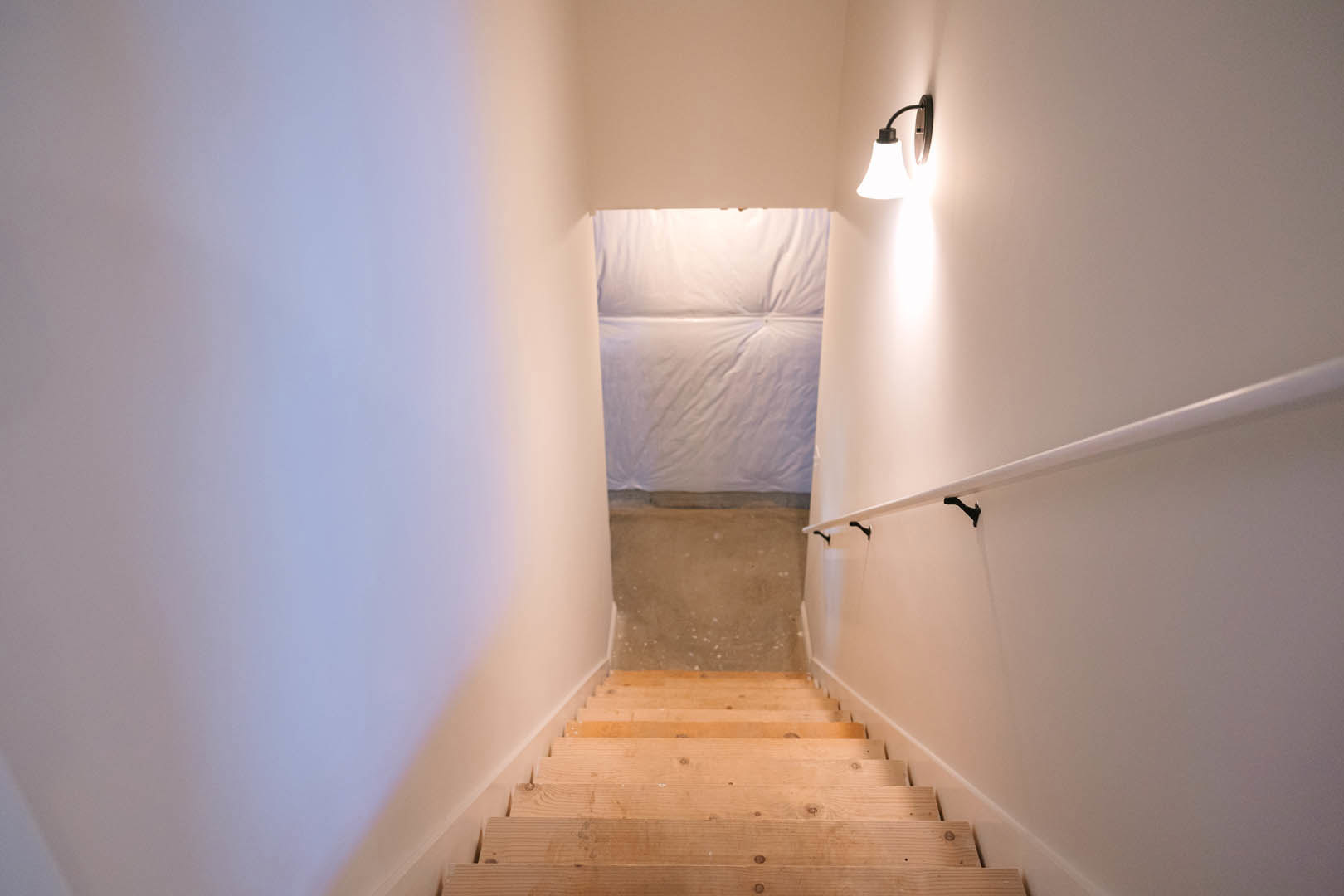 Wooden staircase with warm wall lighting, white plaster walls, and light-toned flooring in a modern residential interior