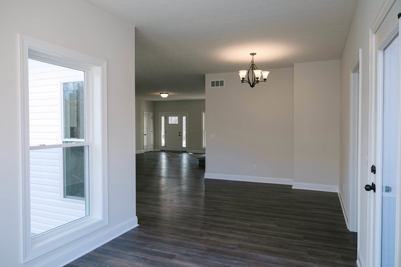 Dark wood flooring, white walls with crown molding, white-framed window, glass-paneled white door, ornate chandelier hanging from ceiling