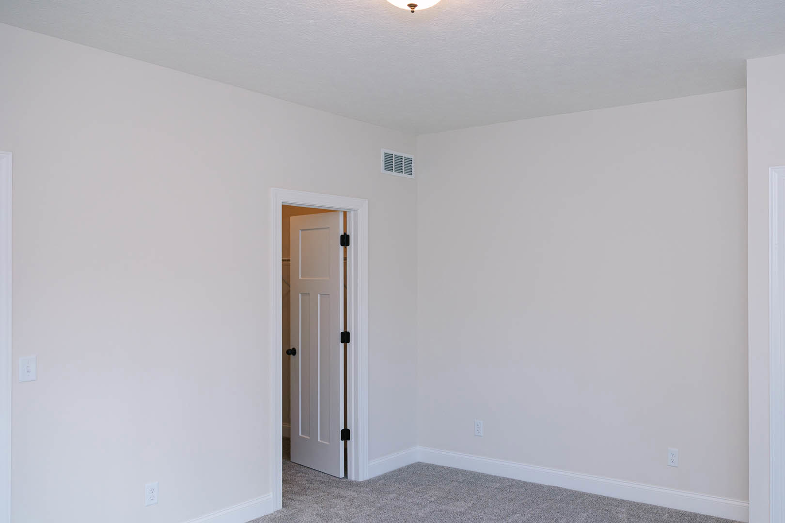 White room with plush carpet, open white door featuring black knobs, recessed ceiling light, wall vent, smooth white walls