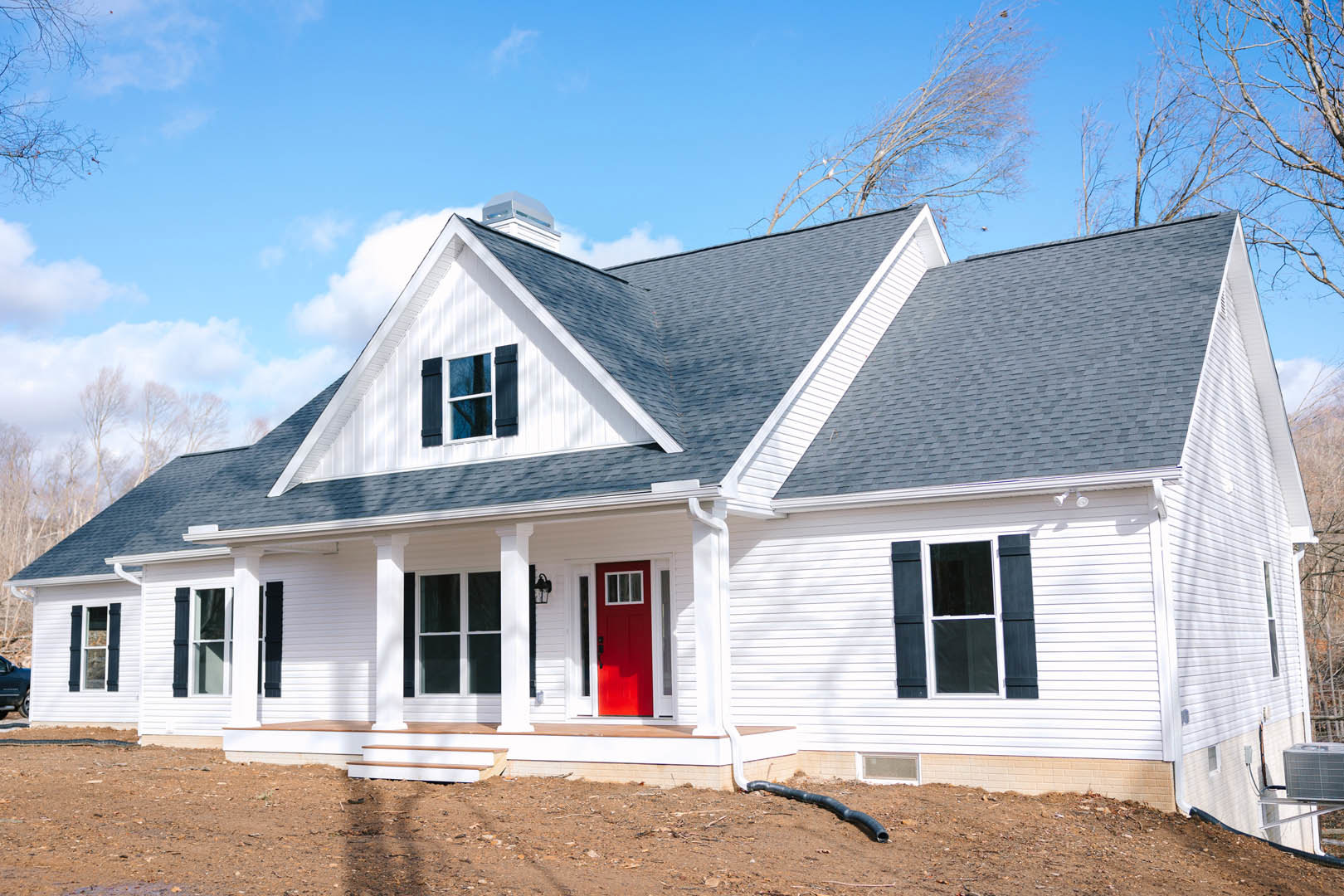 White siding exterior with a red front door, white-framed window, black pipe along the ground, and cloudy sky above
