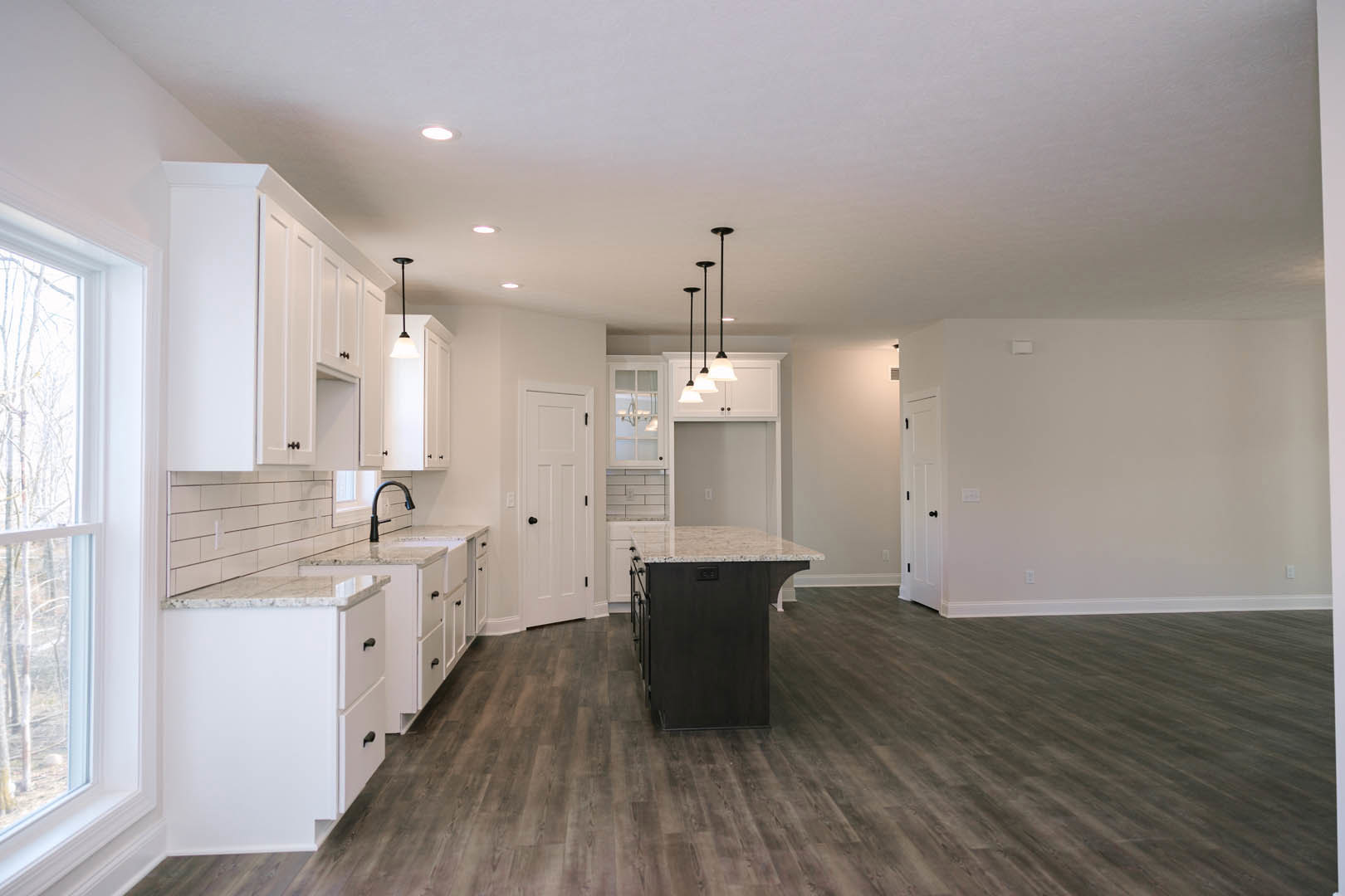 White kitchen cabinets, black marble-topped island, wooden flooring, white countertops with drawers, white door featuring black knob, close-up window visible in background