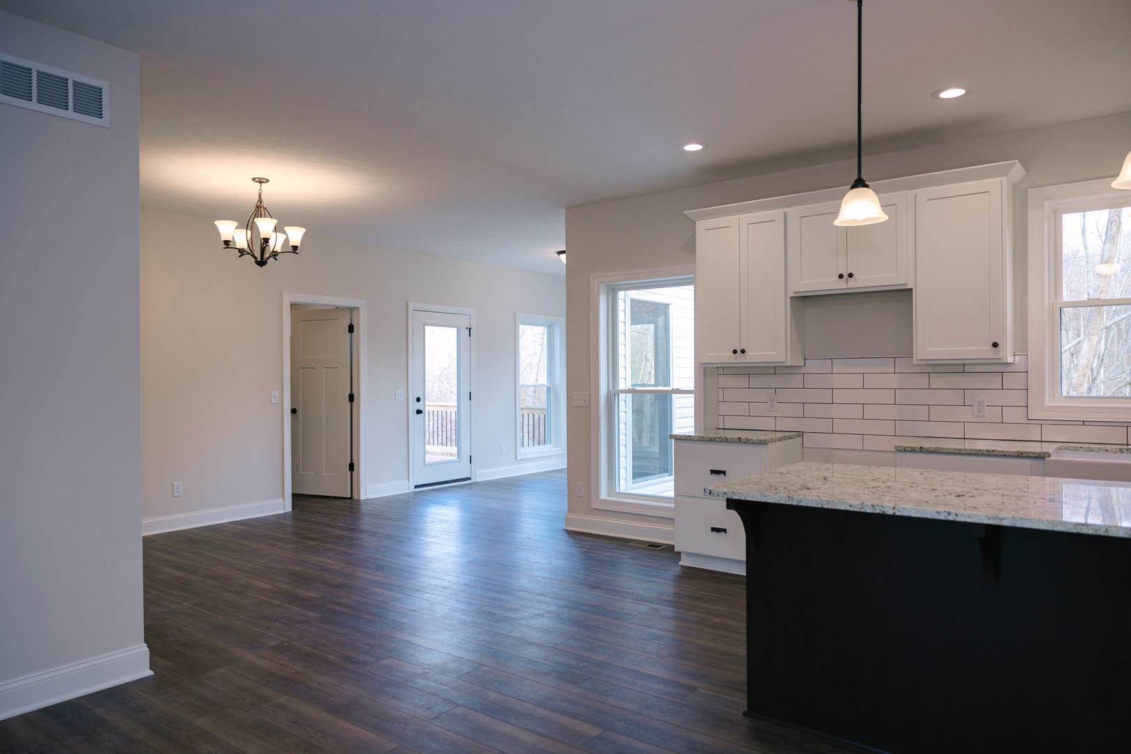 Open kitchen and living room featuring white cabinetry, wood flooring, black and white countertops, glass-paneled white door, five-light chandelier, white door with black knobs