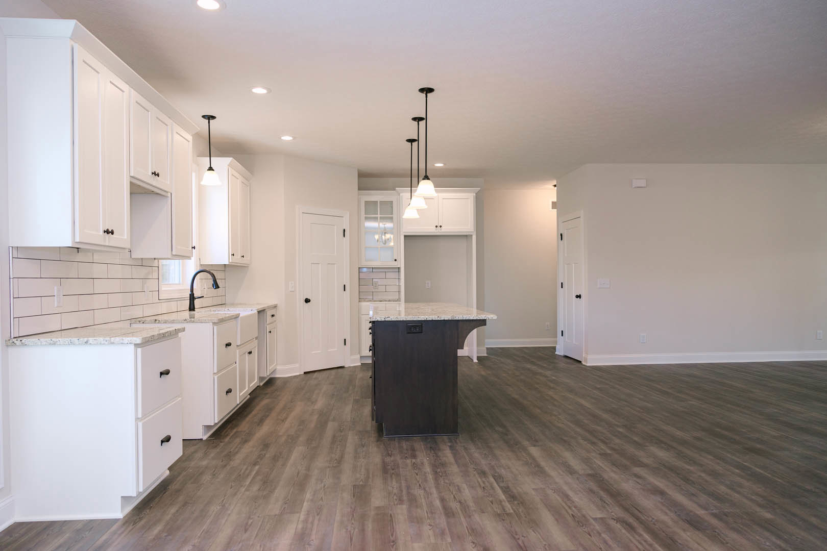White kitchen cabinets, marble-topped island, wood flooring, white countertop with black handles, white door with black knobs, modern lamp fixture