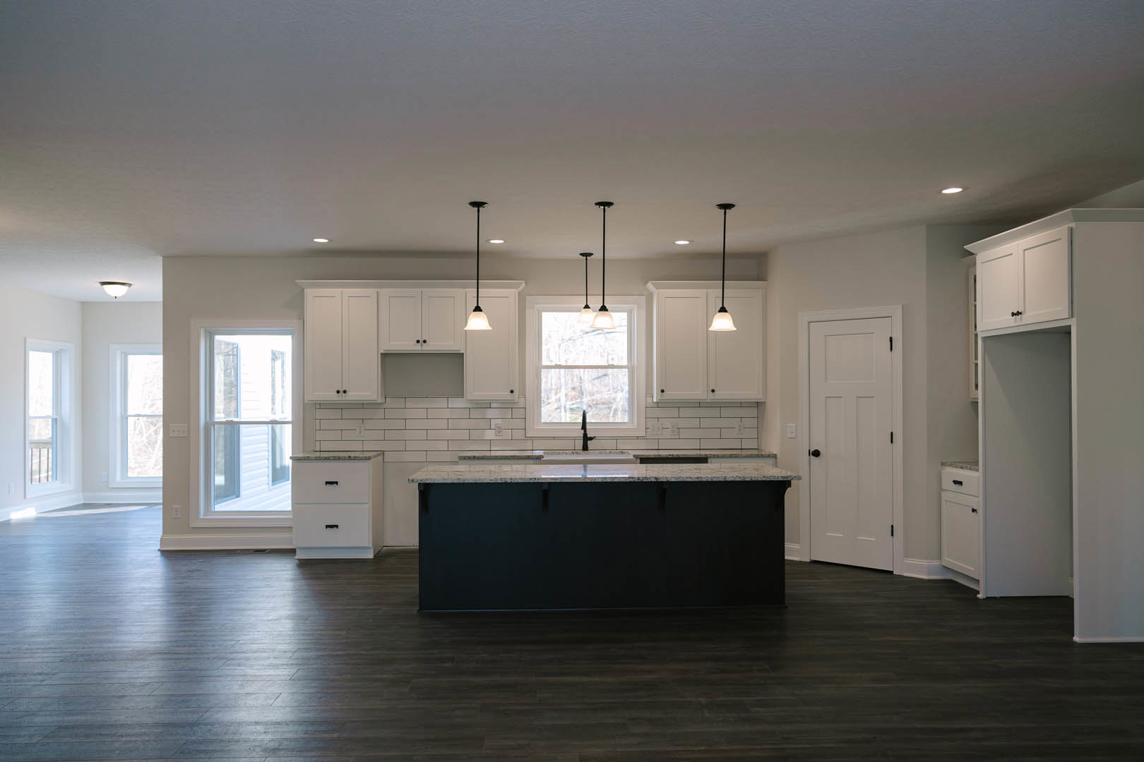 Kitchen featuring a marbled black countertop island with built-in sink, white cabinetry with black handles, white door with black knobs, window with light fixture, and