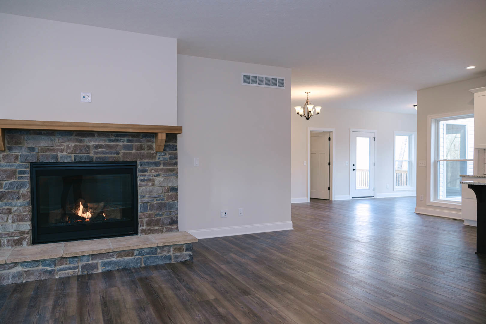 Stone fireplace with burning fire, wood flooring, white door with black handle, modern chandelier, neutral walls