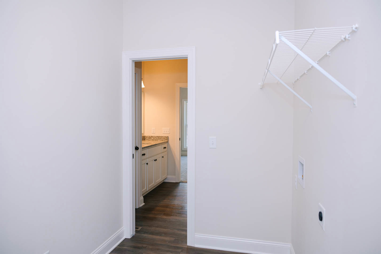 White bathroom with marble countertop, white shelf with hooks, white door, and dark wood flooring with white trim