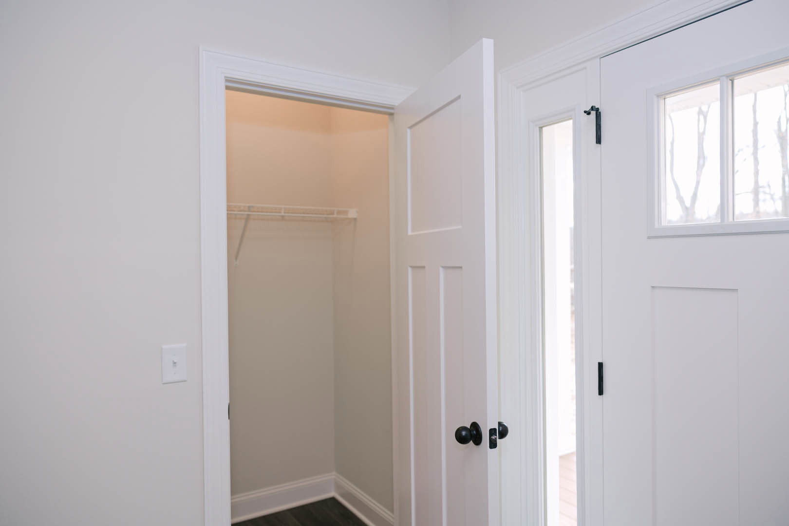 White closet with open door, black handle, white shelf inside, light switch on adjacent white wall, close-up of window nearby.