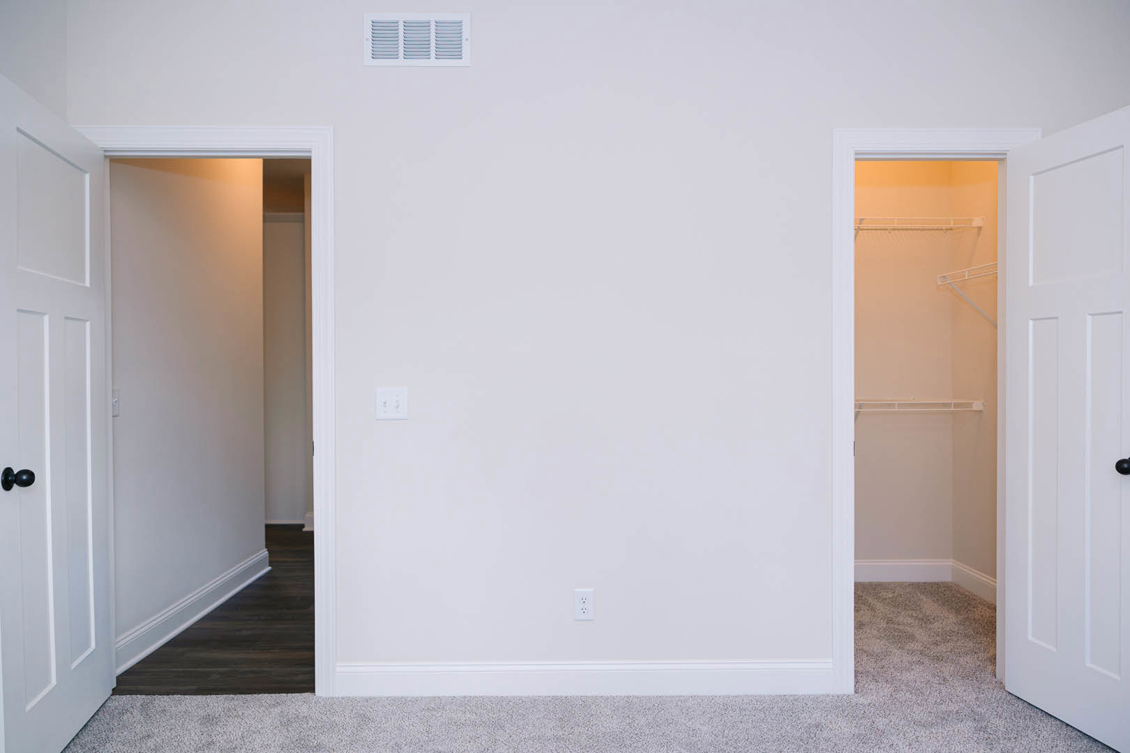 White closet with built-in shelf, white door, and wall-mounted switch, set against smooth plaster walls and light flooring.