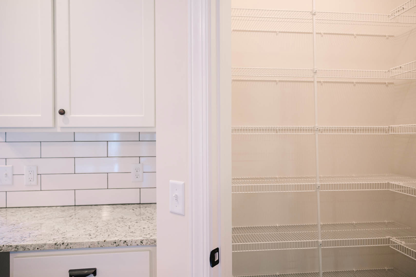 Kitchen featuring white shaker cabinets, white quartz countertops, white tile backsplash with black grout lines, black hardware, and adjacent closet with empty white shelves and a