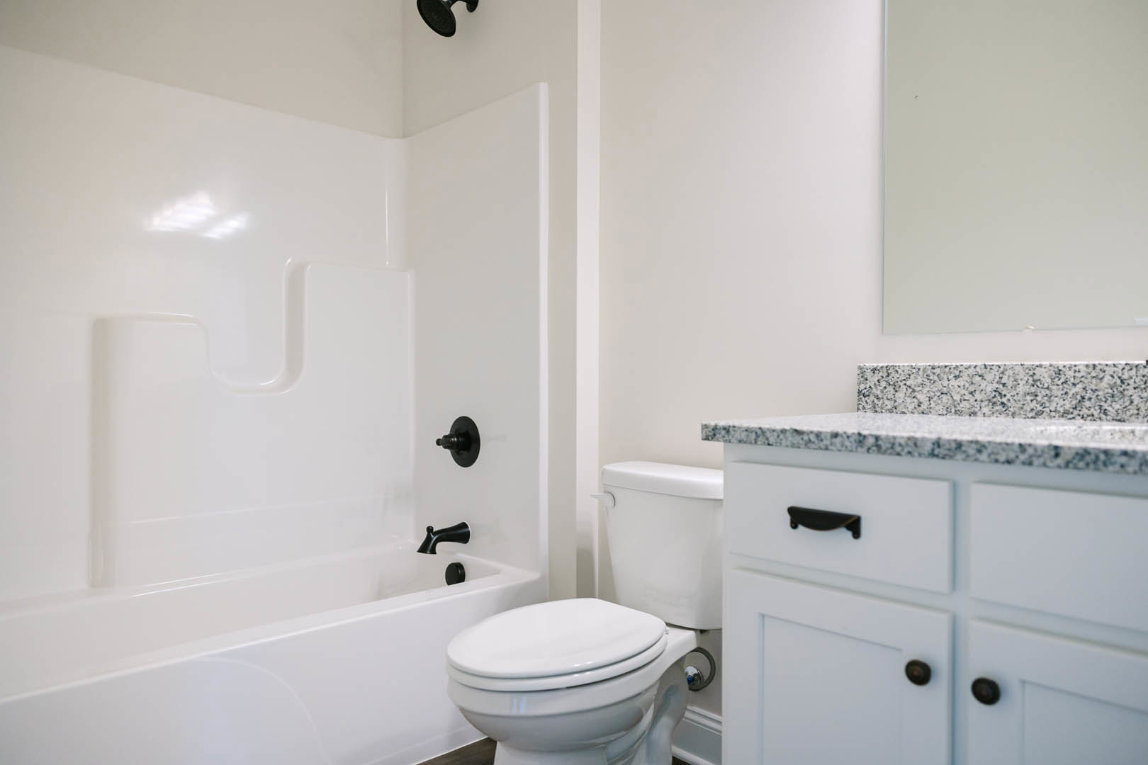White bathroom with freestanding bathtub, modern toilet, black faucet, wall-mounted mirror, and light gray tile flooring