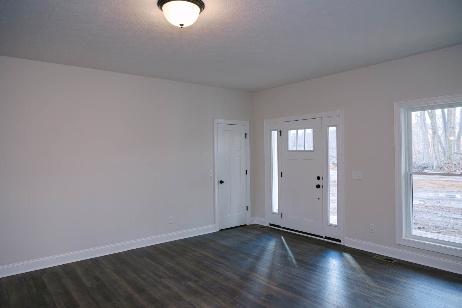 White walls, dark wood flooring, white door with black knobs and glass panes, window overlooking forest