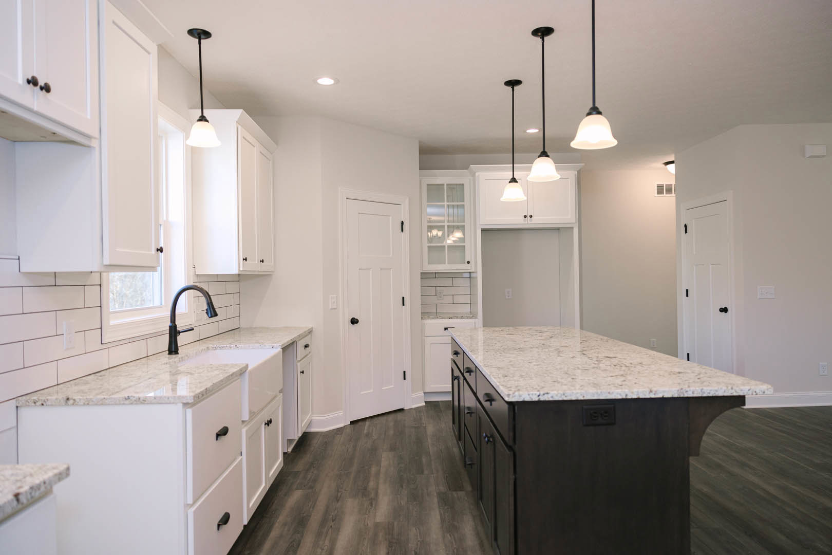 White kitchen cabinets and marble countertops, kitchen island with marble surface, wood flooring with wooden edge, stainless steel faucet, white door with black knobs, window with