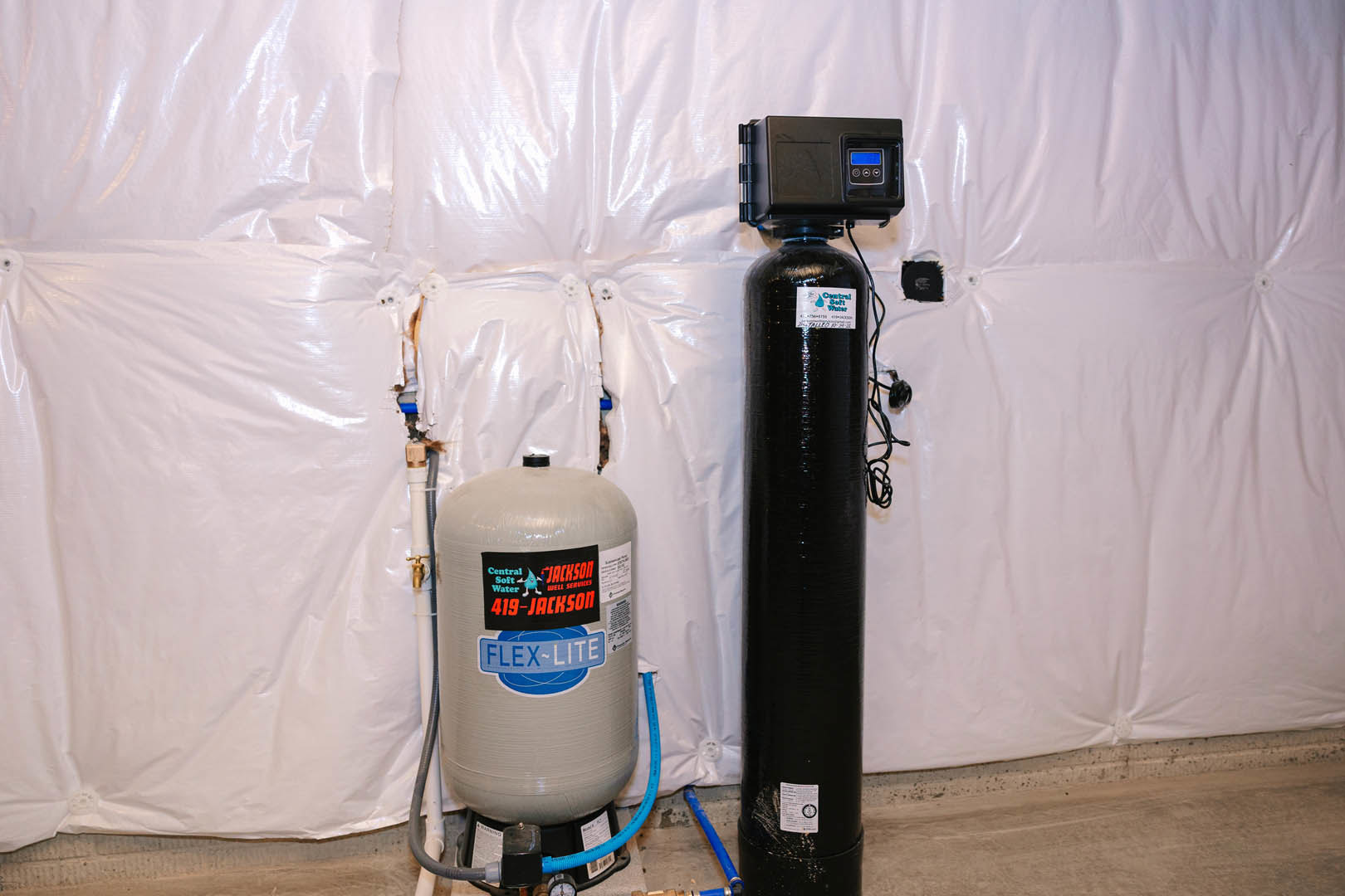 Black and grey cylindrical water tanks with visible wiring and control box mounted on an interior wall