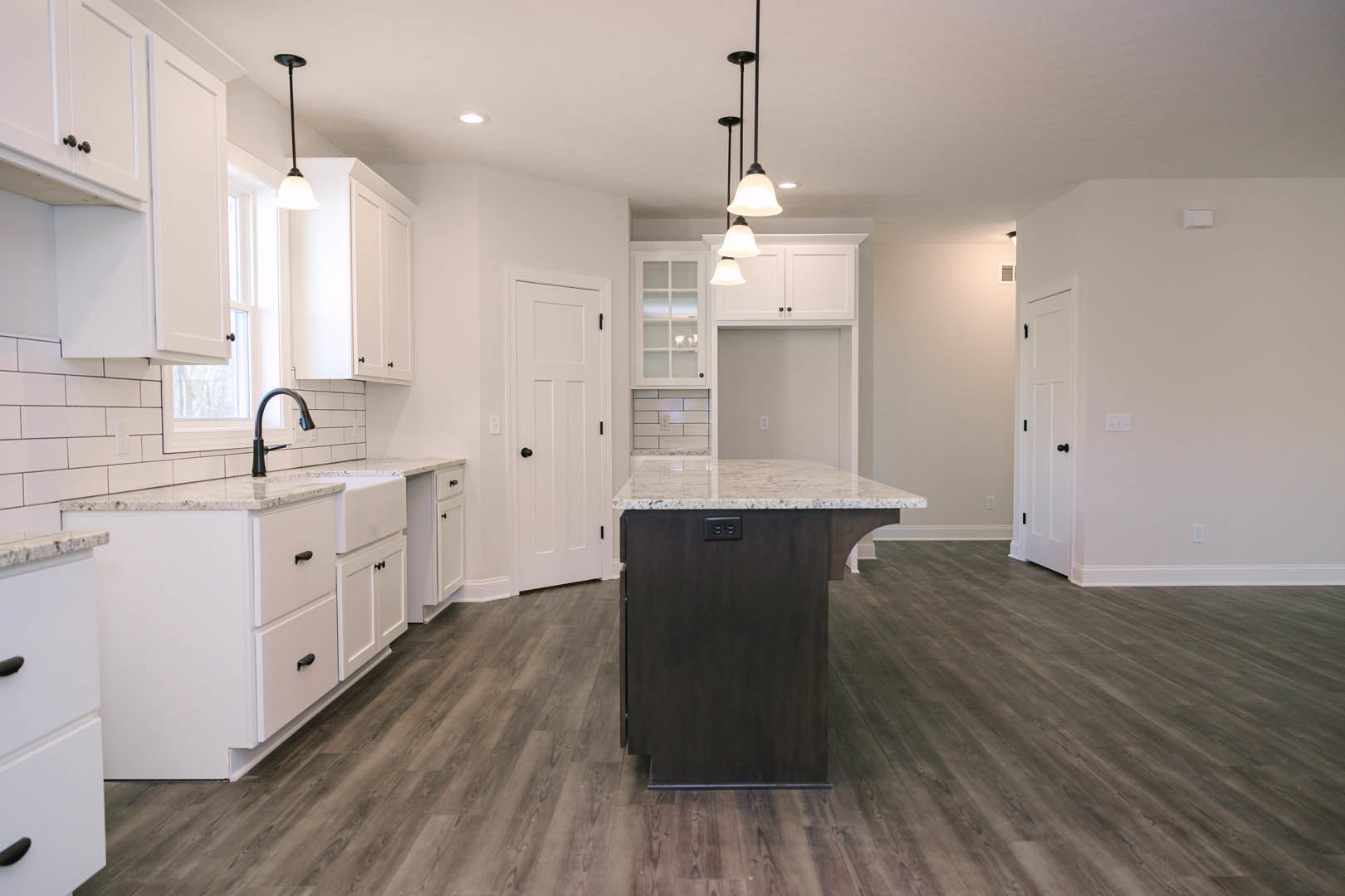 Kitchen with wood flooring, central island featuring marble countertop, white cabinetry, stainless steel faucet, white door with black knob and glass panes