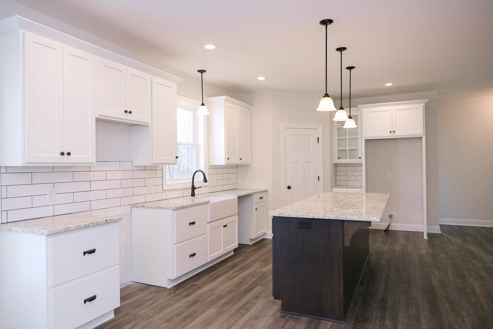 White kitchen with shaker cabinets, white quartz countertops, black hardware, stainless steel faucet, tile backsplash, and light wood flooring