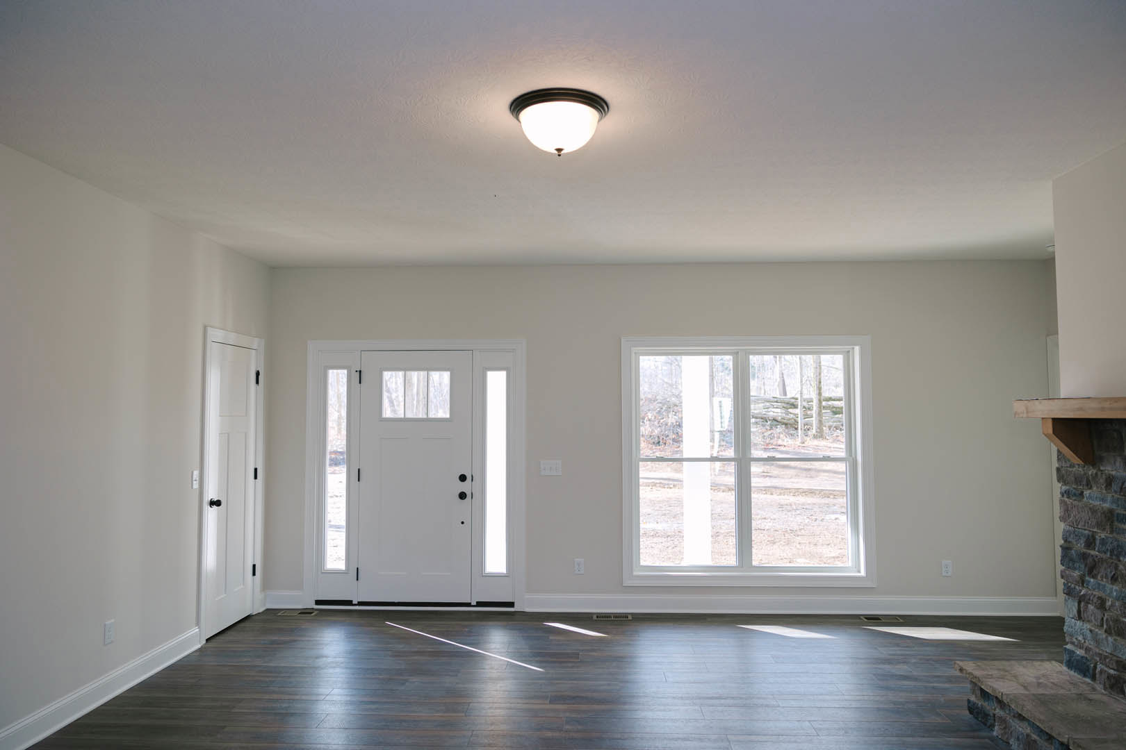 Bright room featuring white paneled doors, large windows with outdoor view, wood laminate flooring with white accents, and a modern ceiling light fixture