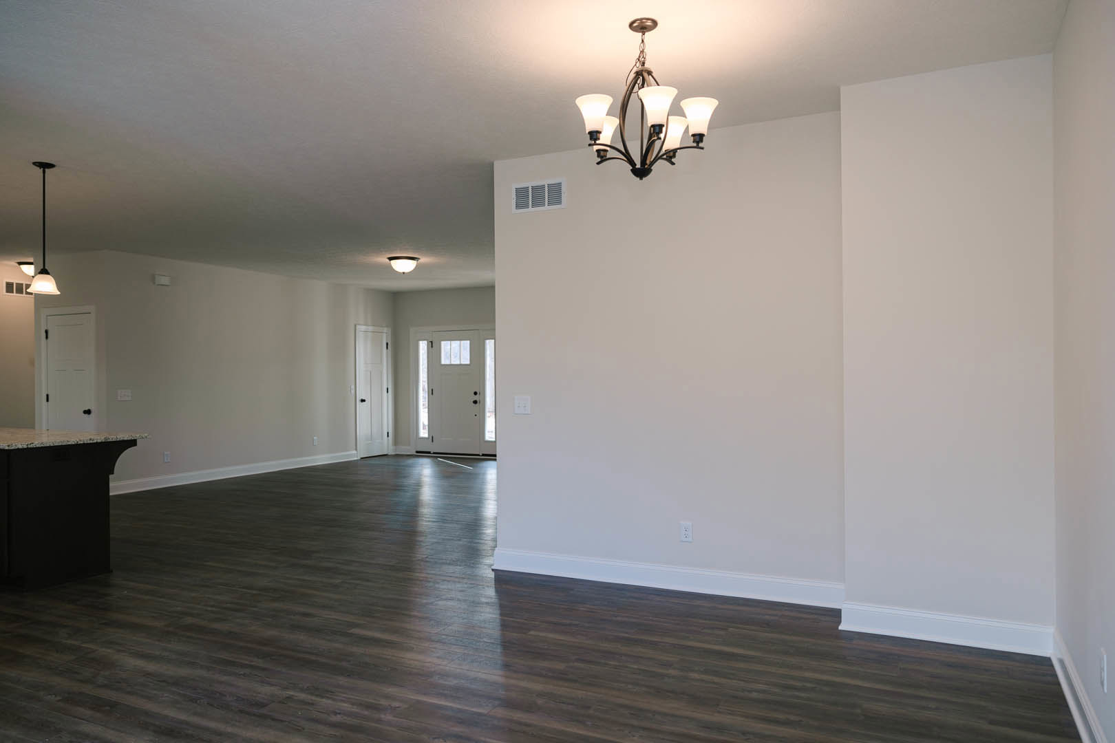 Chandelier with five lights hanging from white ceiling, hardwood floor, white door with glass panes and black knobs, vent on light-colored wall, close-up of stone countertop