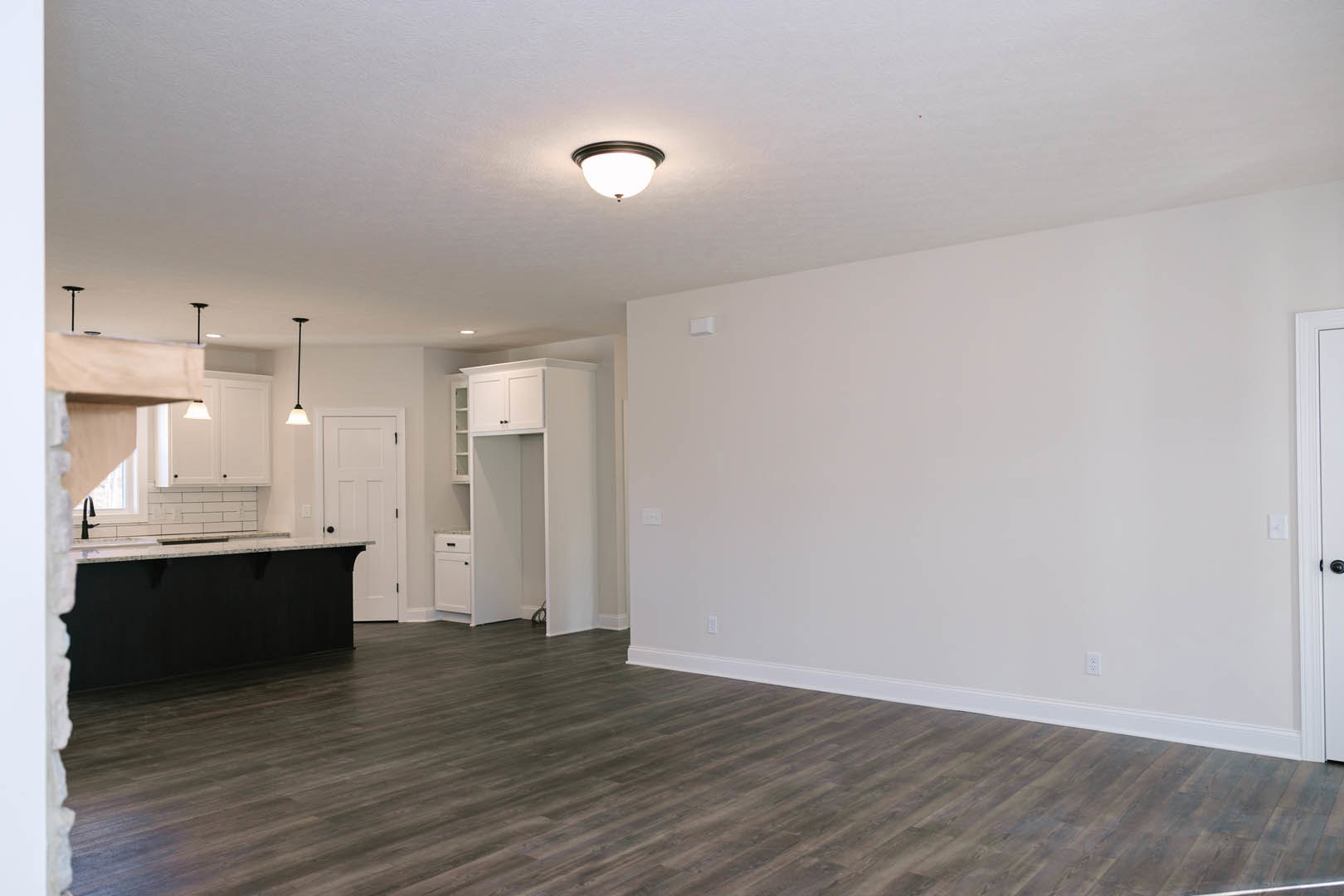 Open kitchen with white cabinetry, marble countertop, wood flooring, white walls, black accent wall with white trim, and modern ceiling light fixture.