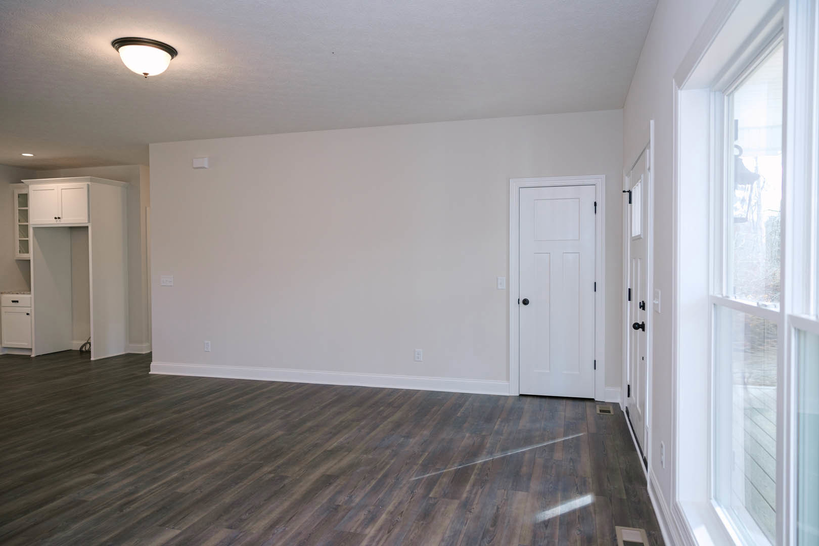 Hardwood floor room with white walls, white door featuring black knobs, ceiling light fixture, white cabinet with black handle