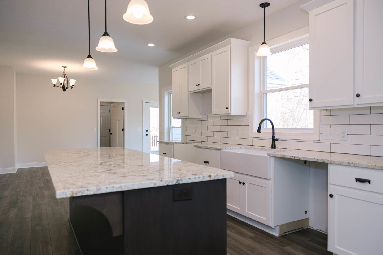 Kitchen with white shaker cabinets, granite countertops, marble-topped island, stainless steel sink, black hardware, tile backsplash, and pendant light near a window
